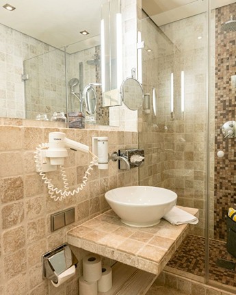 Modernes Bad mit großzügiger Dusche und elegantem Steinfinish Dusche, Waschbecken und Spiegel im Hotelbadezimmer