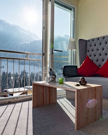 Finden Sie Ruhe und Geborgenheit im Doppelzimmer mit Alpenblick Sitzecke im Hotelzimmer vor Panoramafenster, Wanderrucksack in der Ecke