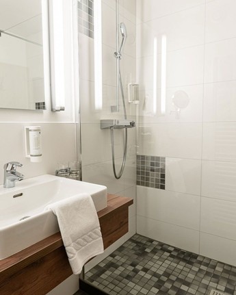 Dusche, Waschbecken und Spiegel im Hotelbadezimmer