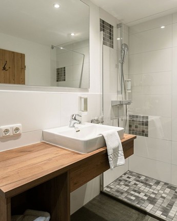 Luxuriöses Badezimmer mit Holzakzenten Dusche, Waschbecken und Spiegel im Hotelbadezimmer