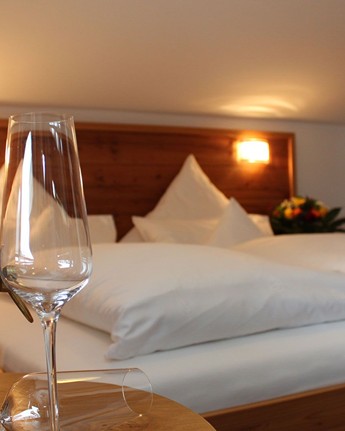 Sektflasche & -glas auf einem Tisch vor dem Bett eines Hotelzimmers