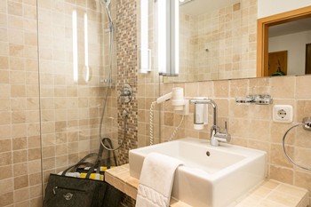 Dusche, Waschbecken und Spiegel im Hotelbadezimmer