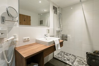 Dusche, Waschbecken und Spiegel im Hotelbadezimmer