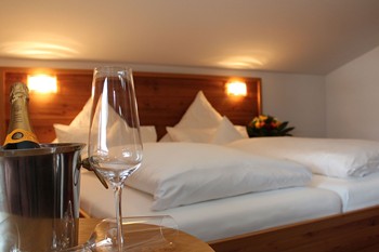 Sektflasche & -glas auf einem Tisch vor dem Bett eines Hotelzimmers