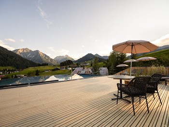 Dachterrasse mit Infinity Pool, Stühlen und Sonnenschirmen mit Blick auf die Berge