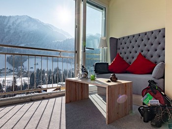 Finden Sie Ruhe und Geborgenheit im Doppelzimmer mit Alpenblick Sitzecke im Hotelzimmer vor Panoramafenster, Wanderrucksack in der Ecke