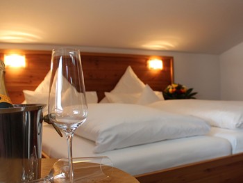 Exklusive Suite mit modernem Holzdesign und Bergblick Sektflasche & -glas auf einem Tisch vor dem Bett eines Hotelzimmers